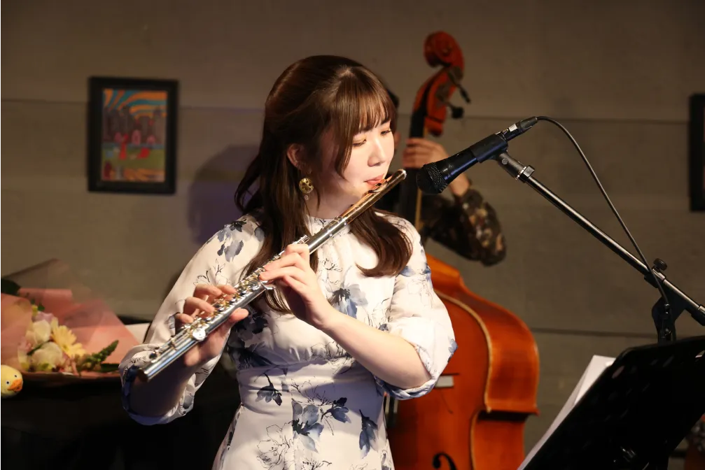シックなライブハウスのステージでフルートを演奏する永田梨紗の写真