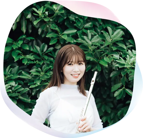 永田梨紗が一面に茂った緑の植物の前でフルートを持って柔らかな笑顔で立っているプロフィール写真